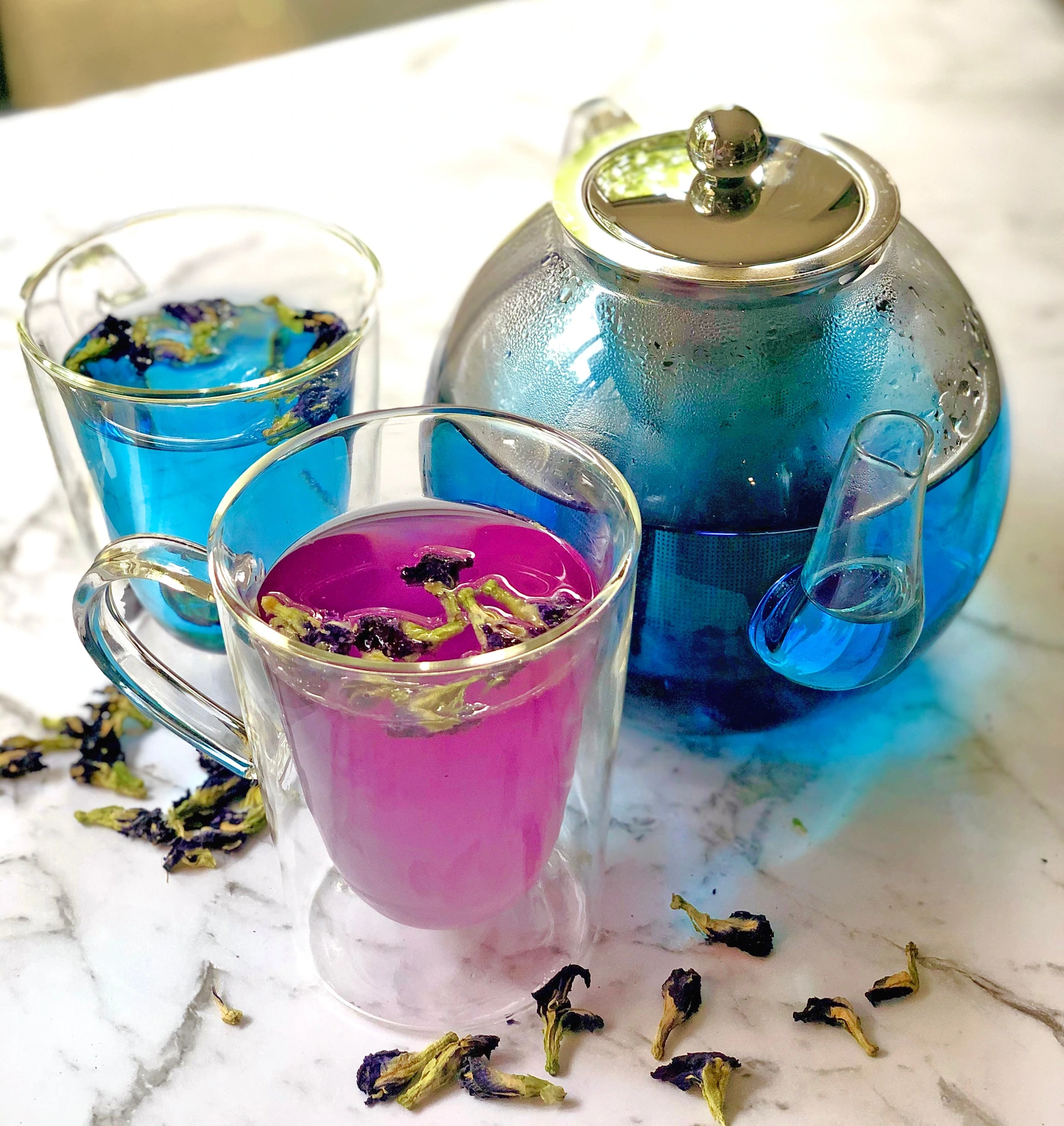 Butterfly pea tea brewed blue, with blue and purple cups